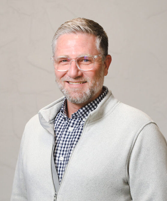 Breakthrough CEO Rev. Andy Houltberg smiles at the camera. He is wearing a great sweater with a blue shirt underneath.